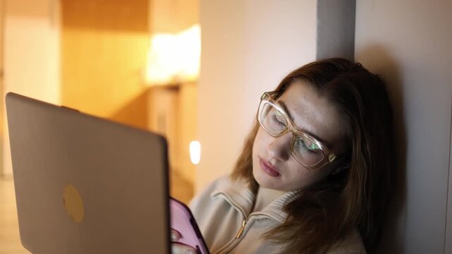 Woman losing focus while working on laptop scrolling smartphone at home evening digital distraction multitasking productivity drop tired routine screen time concept