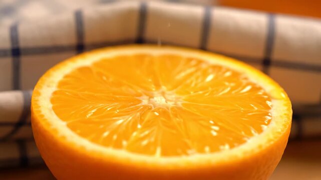 Close-up view of a juicy orange half with vibrant segments and pulp displayed against a blurred background featuring a checkered cloth and suggesting freshness and healthy food preparation