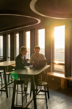 Two men having a business meeting in an office at sunset with coffee and a laptop