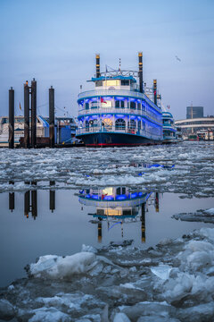Illuminated excursion boat reflecting in icy Hamburg harbor at dusk