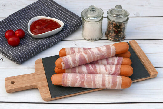 Berner W&uuml;rstchen: Mit Speck ummantelte W&uuml;rstchen auf Schieferplatte mit Tomaten und Gew&uuml;rzen dekoriert.