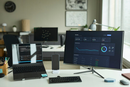Modern office desk with financial dashboard on monitor and laptop