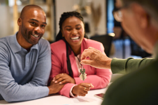 Real estate agent giving house keys to happy black couple
