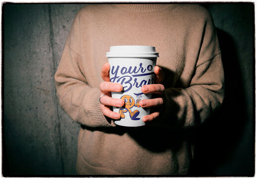 Hands holding blank coffee cup mockup with cozy sweater in moody lighting