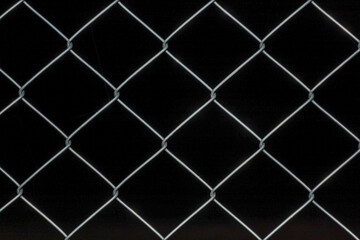 Fototapeta premium Metal chain-link fence with diamond-shaped links creates a sharp geometric pattern against a deep black background. This durable construction is used for fencing territories, providing reliable protec