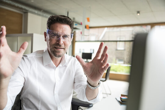 Confident mature businessman gesturing and wearing smart glasses sitting at office