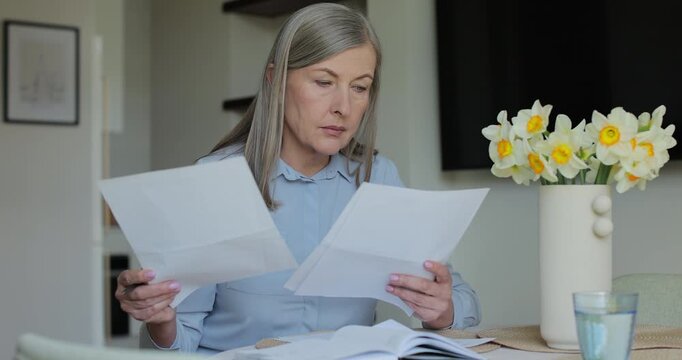 Senior woman filling out financial statements. Older mature lady reading paper bill pay online at home.