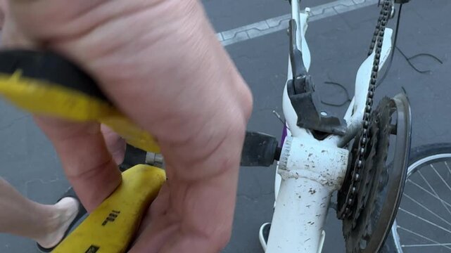 Hands use pliers for bicycle pedal repair and bike maintenance on a white crank in outdoor closeup, showing pedal replacement, diy service and mechanical transport upkeep.