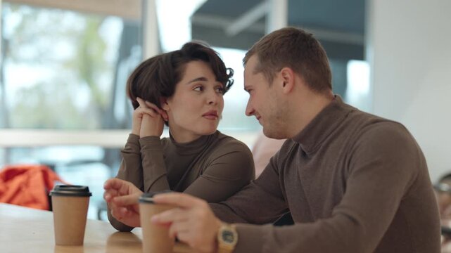 Happy Young Couple Laughing and Talking Over Coffee in a Bright, Modern Cafe