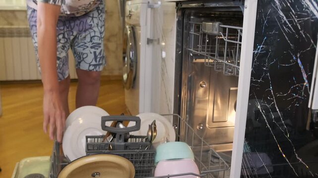 Woman placing dirty plates and utensils into dishwasher in kitchen. Domestic routine, dishwashing preparation, home cleaning process, organizing cookware before washing, everyday household activity.