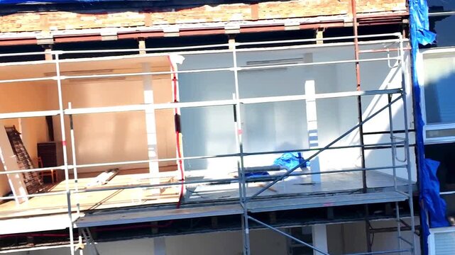 Exterior building renovation with scaffolding and blue tarp protection. Scaffolding surrounds a building undergoing exterior renovation, with blue tarps covering exposed areas and construction