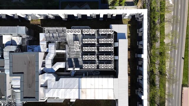 Air conditioning units on the rooftop of a modern office building, showcasing a grid layout with visible ductwork and surrounding urban landscape elements in a clear, sunny environment. Aerial view