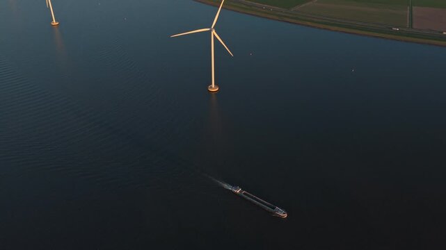Incredible aerial perspective of a large cargo ship navigating through a vast offshore wind farm during a serene sunset in the netherlands