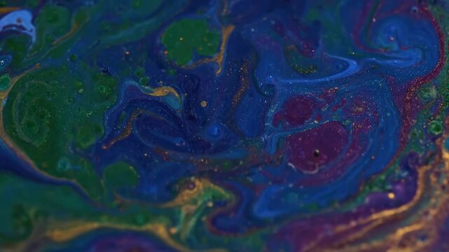 Abstract swirling patterns of deep purple blue and green paint with shimmering gold accents and a glitter effect creating a luxurious cosmic background