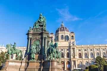 Obraz premium Maria Theresa Monument in Vienna, Austria, featuring bronze statues and horses set before the ornate dome and classical stone facade of the Natural History Museum under clear blue sky