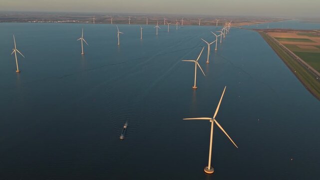 Aerial view of a large offshore wind farm with turbines spinning to produce clean, renewable energy. A cargo barge sails on the water