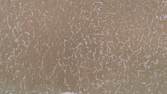 Abstract aerial perspective of moving water textures, beach sand, and coastal leisure activities