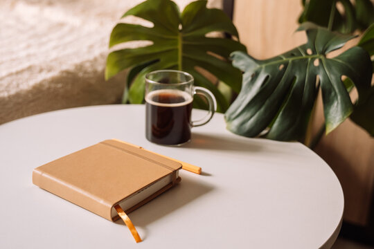 Closed notebook with pen and coffee on round white table.