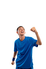 Naklejka premium Enthusiastic young Indonesian southeast asian man wearing a blue sports t-shirt and wristband, looking up and cheering with a clenched fist, celebrating a win or success against a white background