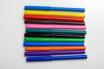 Fototapeta premium Top view of a collection of vibrant felt-tip pens in various colors neatly arranged horizontally on a white surface. Perfect for art, education, and creative design project concepts
