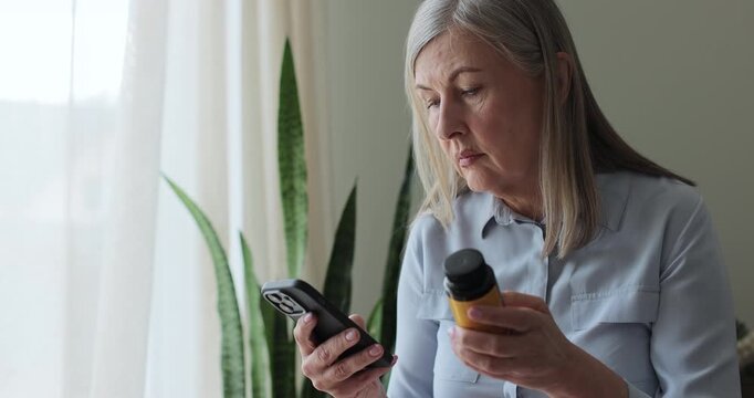 Elderly woman uses phone for online research on pills, searching medication information on the internet at home. Search side effects and online for drug info website for dosage instructions, check