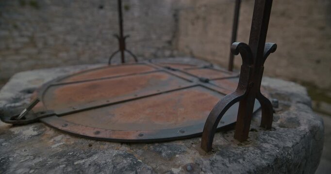 A close view shows a stone well with a rusted metal lid and iron support elements in a courtyard.