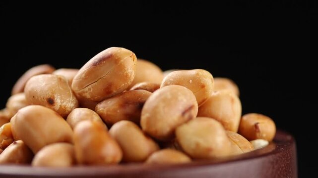 Pile of roasted hulled peanuts on wooden bowl rotating on black background. 
