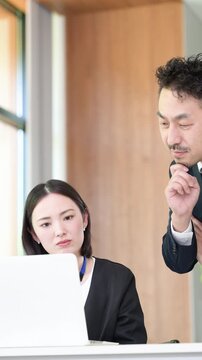 パソコンの前で真剣な表情で考える悩むデスクワーク業務に取り組む上司と部下の男女のビジネスマンチーム　この問題、課題どうしようかな～の縦動画