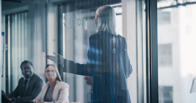 Business Leader Stands at the Front of a Glass Walled Conference Room, Leading a Strategy Meeting Where Colleagues Listen, Share Ideas, Review Performance Updates, and Coordinate Upcoming Projects