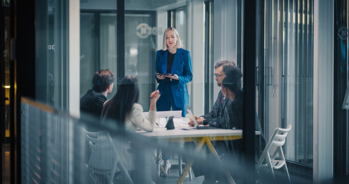 Female Executive Leads a Strategic Business Meeting in a Glass Office, Using a Digital Tablet to Guide Discussion While Colleagues Review Documents, Share Ideas, Analyze Performance, and Coordinate