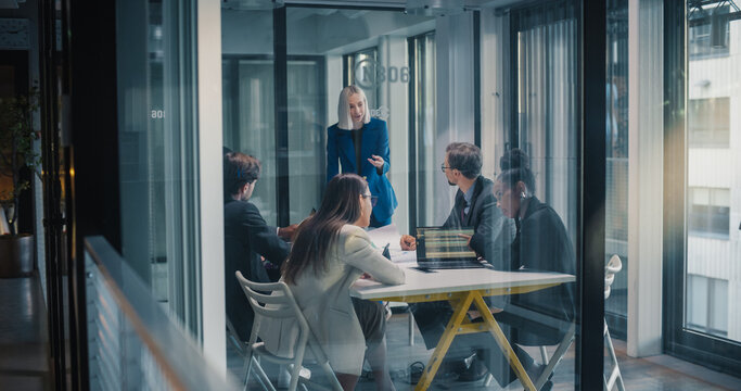Business Professionals Hold a Strategy Meeting in a Glass Office as a Female Leader Presents Key Insights, Reviews Digital Dashboards, Clarifies Priorities, Manages Risks