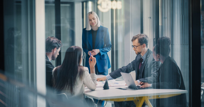 Female Executive Leads a Focused Business Meeting in a Glass Office, Guiding a Team Through Strategy Review, Financial Planning, and Project Coordination While Colleagues Analyze Reports, Share Ideas