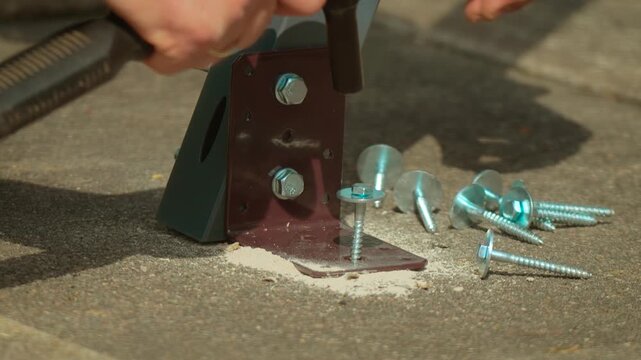 Metal bracket fastening to concrete base with screws driving into plastic anchors close up. Ratchet wrench tightening fasteners securing construction element to masonry surface. Installation process