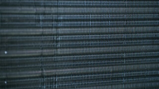 Detailed macro view of the intricate metal fins and cooling tubes of an automobile engine radiator, showing the texture and pattern of the heat exchanger component with a smooth sliding movement