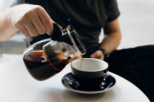Man pouring pu erh tea from glass teapot into cup. Cozy home tea ritual.