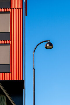 Lamp under blue sky beside modern minimal architecture facade shows red lines detail creating clean urban backdrop for signage and branding