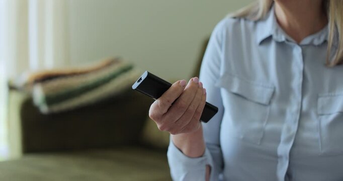 Close up shot of a senior woman hand holding modern TV remote control. Channel surfing. Watching Online cinema.