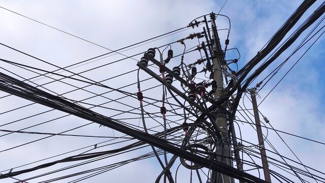 Complex network of power lines and utility pole against cloudy blue sky. Intricate electrical infrastructure. High voltage wires