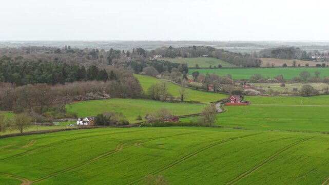 Patchwork farmland panorama with village settlement and rolling green fields under dramatic cloudy sky. Aerial perspective revealing agricultural land patterns hedgerows rural housing clusters and