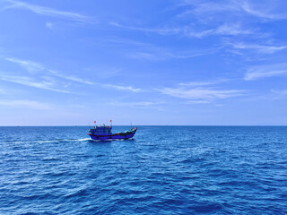 Obraz premium Distant view of a blue vessel cruising on the wide blue ocean