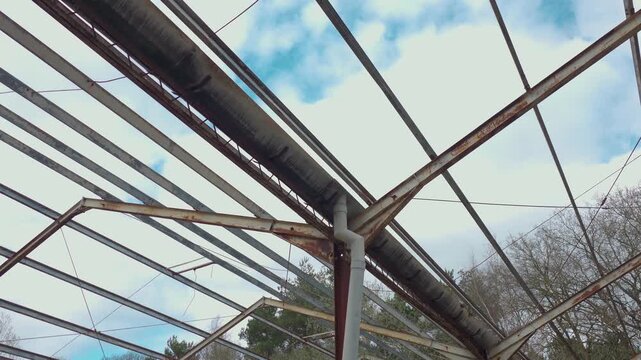 Empty military warehouse roof remains with exposed iron trusses and damaged infrastructure. Looking upward across deteriorating metal grid pipes and structural elements in abandoned hangar setting