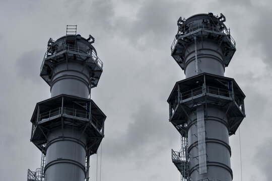 Industrial chimney and metal towers at a power plant beneath clouds with vertical energy forms showcasing engineering and infrastructure