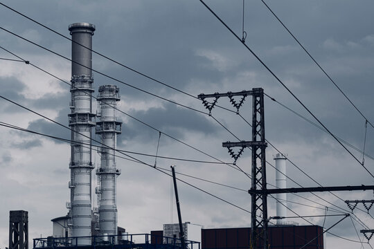 Chimney above rail wires near an overcast industrial plant where urban energy networks define Frankfurt city infrastructure and skyline