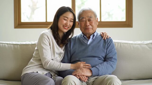 Younger adult in knitwear gently embraces an older adult on a light sofa, exchanging warm smiles in a serene, naturally lit home with blurred decor. Concept of intergenerational love and care