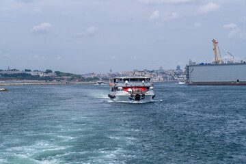 Fototapeta premium Cruise boat moves along the Bosphorus Strait, showcasing Istanbuls skyline and the vibrant maritime activity on a sunny day.