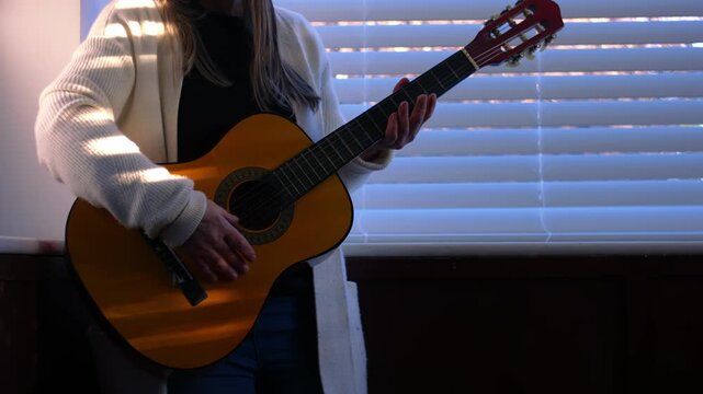 Woman picks up acoustic guitar in window light