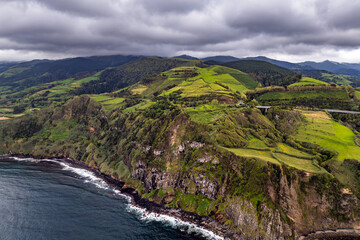 Rocky Atlantic coastline of Azores with green agricultural fields on cliff, aerial view of coastal farmland and ocean waves © Leonid
