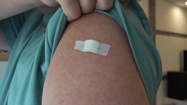 Close-up of an adult person showing a fresh adhesive bandage on the upper arm after receiving a vaccine shot. Real life healthcare concept of seasonal vaccination. 