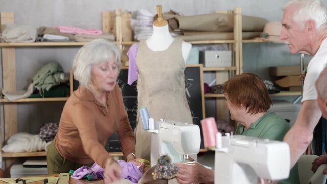  Elderly female teacher shows group of elderly people how to sew clothes on mannequin at master class