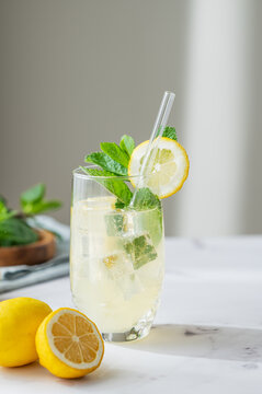 A refreshing summer drink with lemon, mint, and ice in a glass on a light background.